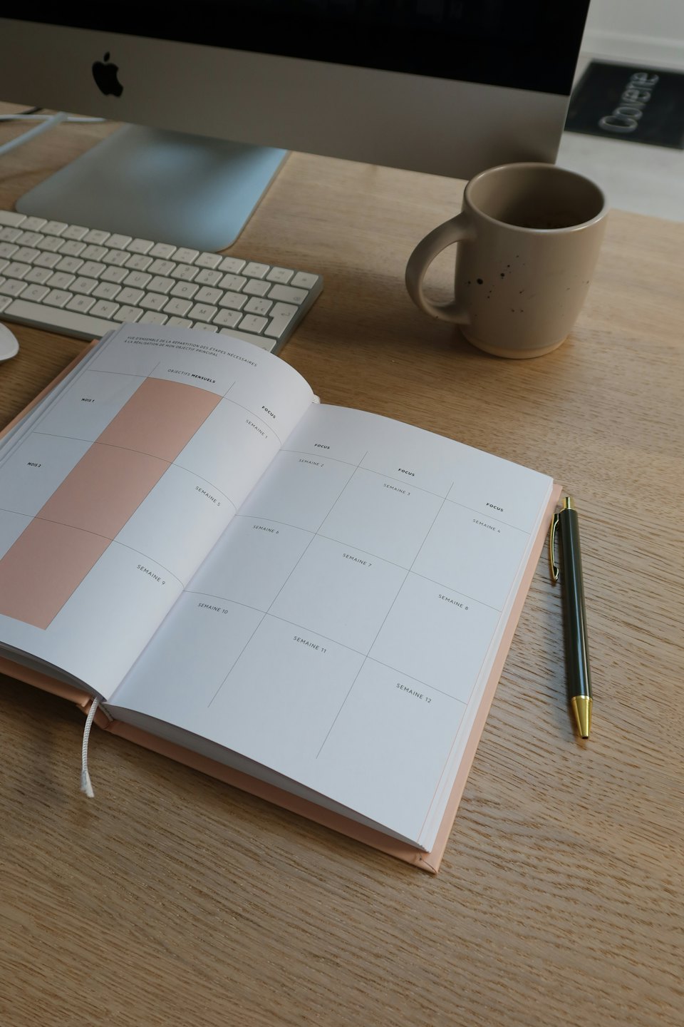 Desk with open planner, pen, mug, and computer.