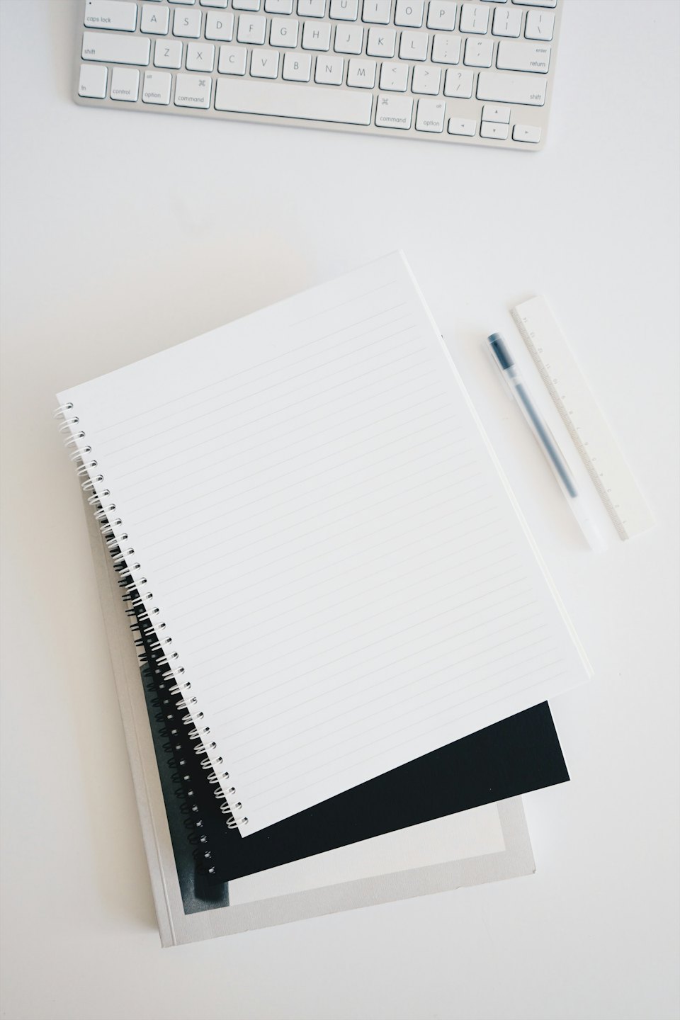 Minimalist workspace with notebooks, pen, ruler, and keyboard.